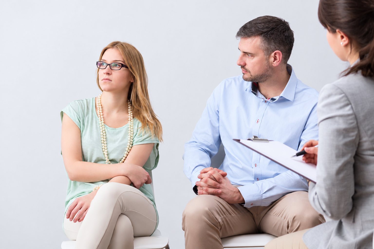 Une femme aux bras croisés et un homme assis détournent le regard lors d'une séance de thérapie de couple avec une conseillère qui prend des notes.
